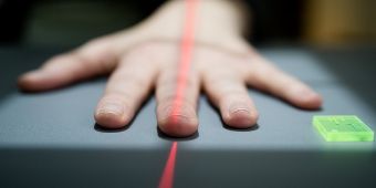 Das Foto zeigt eine Hand, die mit gespreizten Fingern auf einer Ablage liegt. In der Mitte der Hand verläuft ein roter Laser-Strich.