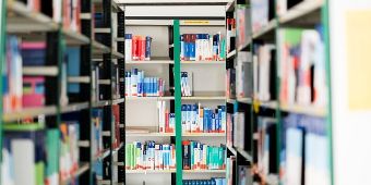 Das Foto zeigt einen Gang unserer Bibliothek mit vielen Regalen, in denen Fachbücher aufgereiht sind. 