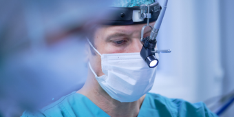 Sektionsleiter Dr. Hartmut Koch im OP Man sieht die Nahaufnahme eines konzentrierten Chirurgen im OP-Saal mit einer Stirnlampe auf dem Kopf.