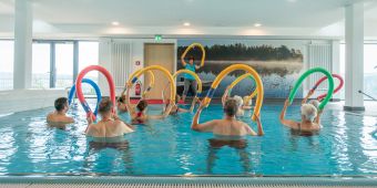 Viele Patienten sind im Bewegungsbad und haben für die Aquagymnastik Poolnudeln in den Händen