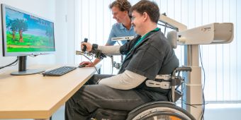 Eine Therapeutin führt am Armroboter Übungen mit einem Patienten durch