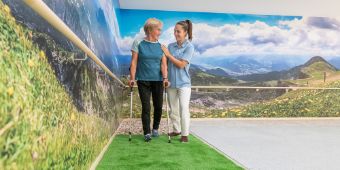 Eine Therapeutin führt Gehübungen mit einer Patienten auf verschiedenen Untergründen durch