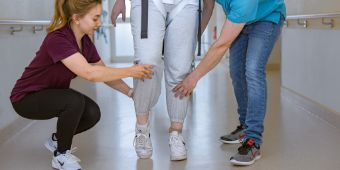 Das Bild zeigt zwei Therapeuten, die den Patienten beim Gehen unterstützen