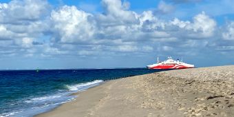 Das Bild zeigt die rot-weiße Syltfähre im Meer vor dem Strand in List.