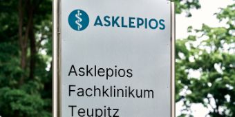 Auf dem Bild ist ein Schild mit dem Logo von Asklepios und dem Schriftzug "Asklepios Fachklinikum Teupitz" zu sehen