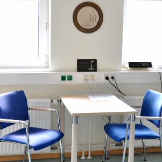 Das Motiv zeigt den Behandlungsraum der Onkologischen Ambulanz mit Tisch und zwei blauen Stühlen.