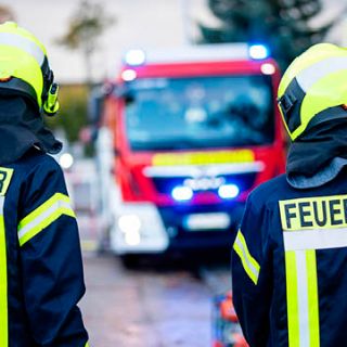 Bild: Feuerwehrleute vor Einsatzfahrzeug mit Blaulicht