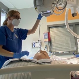 Foto: Medizinische Technologin steht neben einem Patientenbett und fertigt Röntgenaufnahmen an