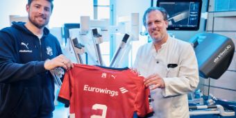 Prof. Dr. Christian Wülfing (rechts) und Tobias Schimmelbauer (links) präsentieren das Trikot, das der Handballer mit dem Operationsroboter signiert hat.