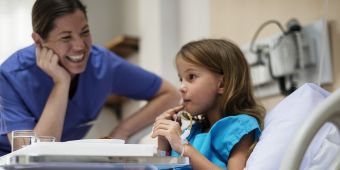 Kinderkrankenpflege Bild: Eine Kinderkrankenpflegerin lacht eine junge Patientin an