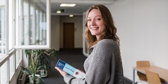 Dein akademischer Weg in die Pflege Lächelnde Studentin auf einem Flur schaut Richtung Kamera