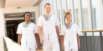 Bild: Drei Pflegefachkräfte laufen nebeneinander über einen Krankenhausflur