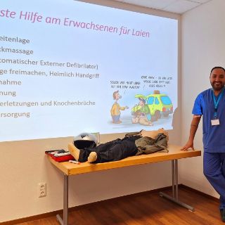 Bild: Referent Hr. Akhundzada mit Übungspuppe und Vortragsfolie zu Erste-Hilfe-Maßnahmen
