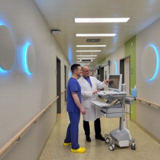 Das Motiv zeigt den Ärztlichen Leiter und eine Pflegefachkraft auf dem Flur der Intensivstation. An den Wänden sieht man die neue Tagesbeleuchtung im Rahmen des Delir-Managements zur Delir-Prävention.