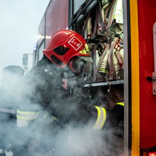 ein Feuerwehrmann kniet vor einem Feuerwehrauto im Nebel (Rauch)