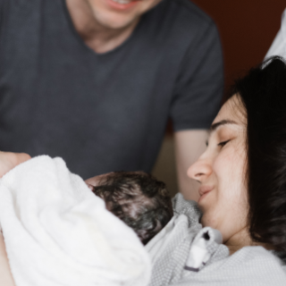Mama und Papa begrüßen das Baby nach der Entbindung. Das Neugeborene liegt bei der Mutter auf der Brust.