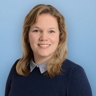 Text: Merle Riedel Porträt Frau mittellange blonde Haare lachend Pullover Dunkelblau Hintergrund blau Asklepios