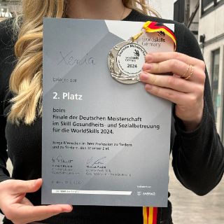 Das Bild zeigt Xenia wie sie eine Urkunde in den Händen trägt.