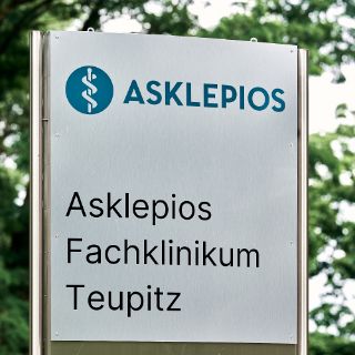 Auf dem Bild ist ein Schild mit dem Logo von Asklepios und dem Schriftzug "Asklepios Fachklinikum Teupitz" zu sehen