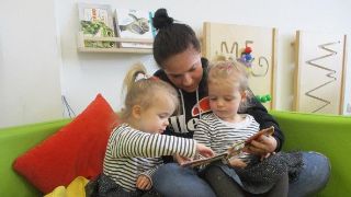 Bild: Erzieherin schaut zusammen mit zwei Kindern ein Buch an