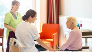 Das Bild zeigt eine Therapeutin und eine Pflegekraft im Gespräch mit einer Patientin