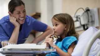 Eine Kinderkrankenpflegerin schaut einer kleinen Patientin beim Trinken zu