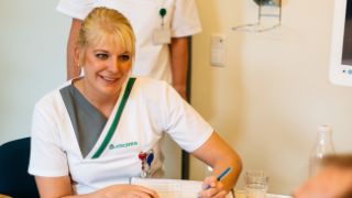 Eine Pflegefachfrau füllt mit einem Patienten einen Anamesebogen aus