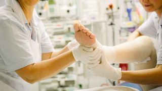Bild: Pfleger hält den Fuß des Patienten für eine physiotherapeutische Übung