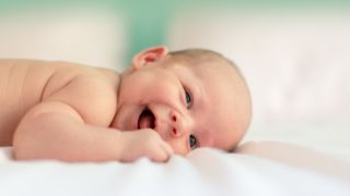 fEin Baby liegt auf dem Bauch und lächelt in die Kamera. Der Fokus liegt auf dem Kind. Der Hintergrund ist verschwommen.