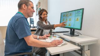 Eine Therapeutin führt mit einem Patienten Übungen am Computer aus