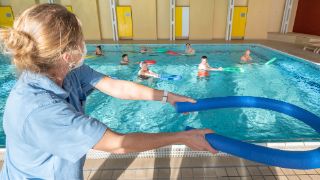 Das Motiv zeigt eine Therapeutin, die Patienten bei der Aquafitness im Bewegungsbad anleitet.