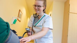 Das Motiv zeigt eine Pflegefachkraft beim Blutdruckmessen.