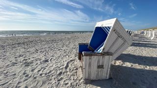Das Bild zeigt einen Strandkorb vor blauem Himmel am Strand.