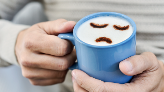 Eine Tasse mit traurigem Smiley wird in der Hand gehalten