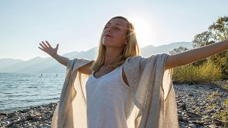 Bild: Glückliche junge Frau steht am Strand mit ausgebreiteten Armen