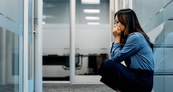 Junge Frau sitzt auf dem Boden um Büro und hat eine Panikattacke