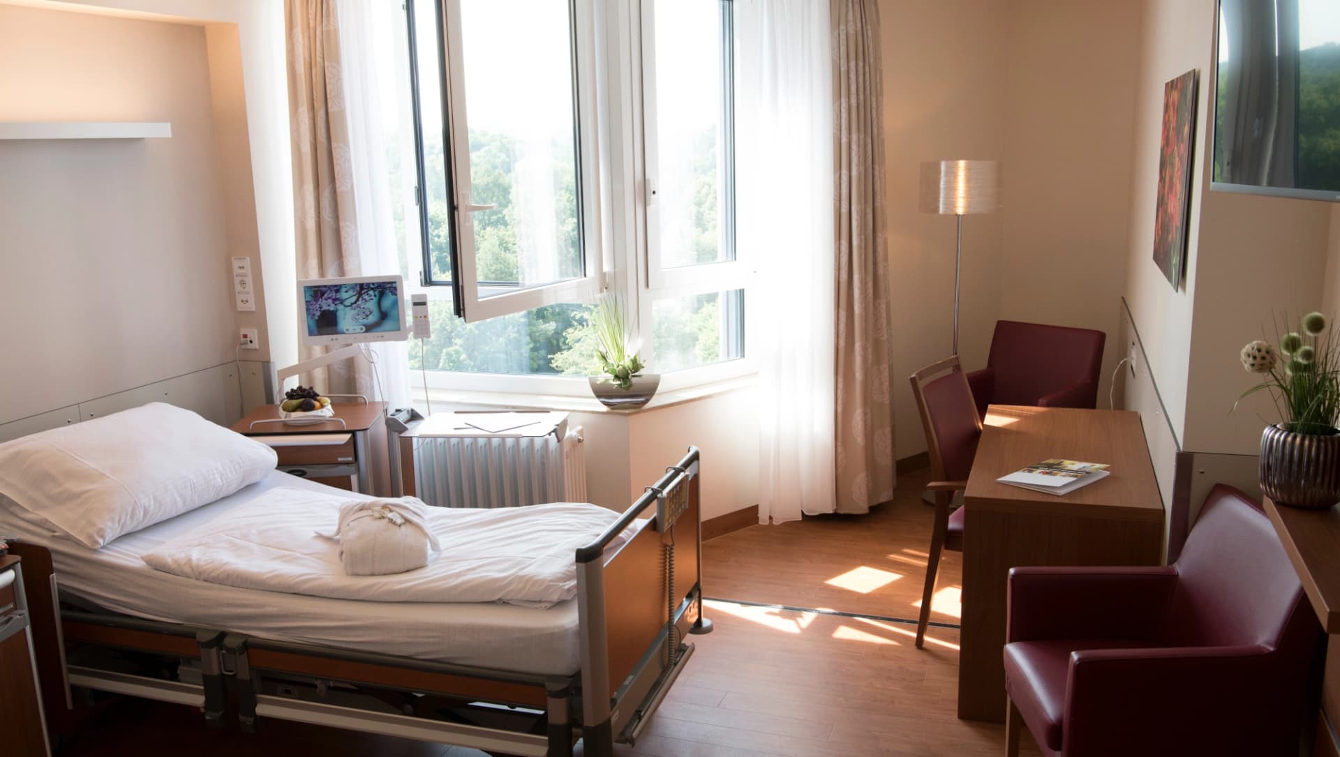 Das Bild zeigt ein lichtdurchflutetes Zimmer der Privatstation mit komfortabler Sitzecke , Privita-Bett inl.  Bedside - Monitor für den Schwesternruf, Telefonie und TV