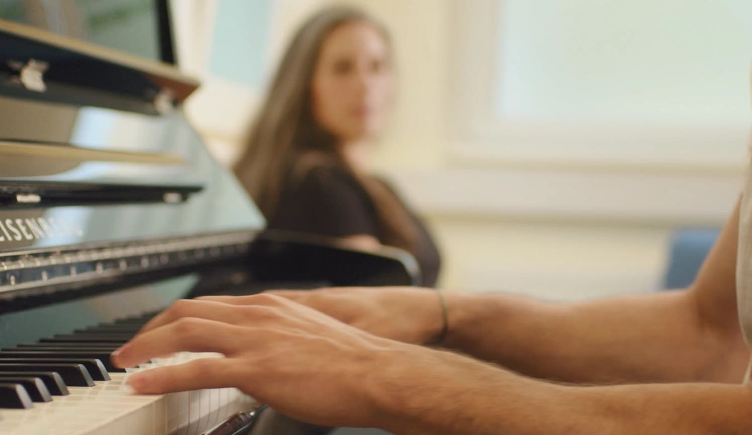 Das Bild zeigt eine Patient:in beim Klavierspielen und eine zuhörende Person