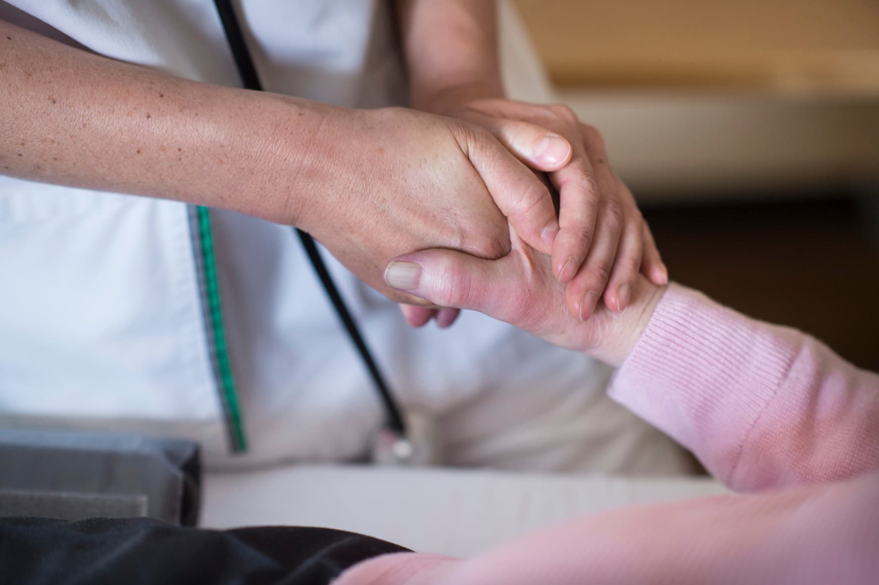 Das Motiv zeigt eine Pflegekraft, welche die Hand einer Patientin hält