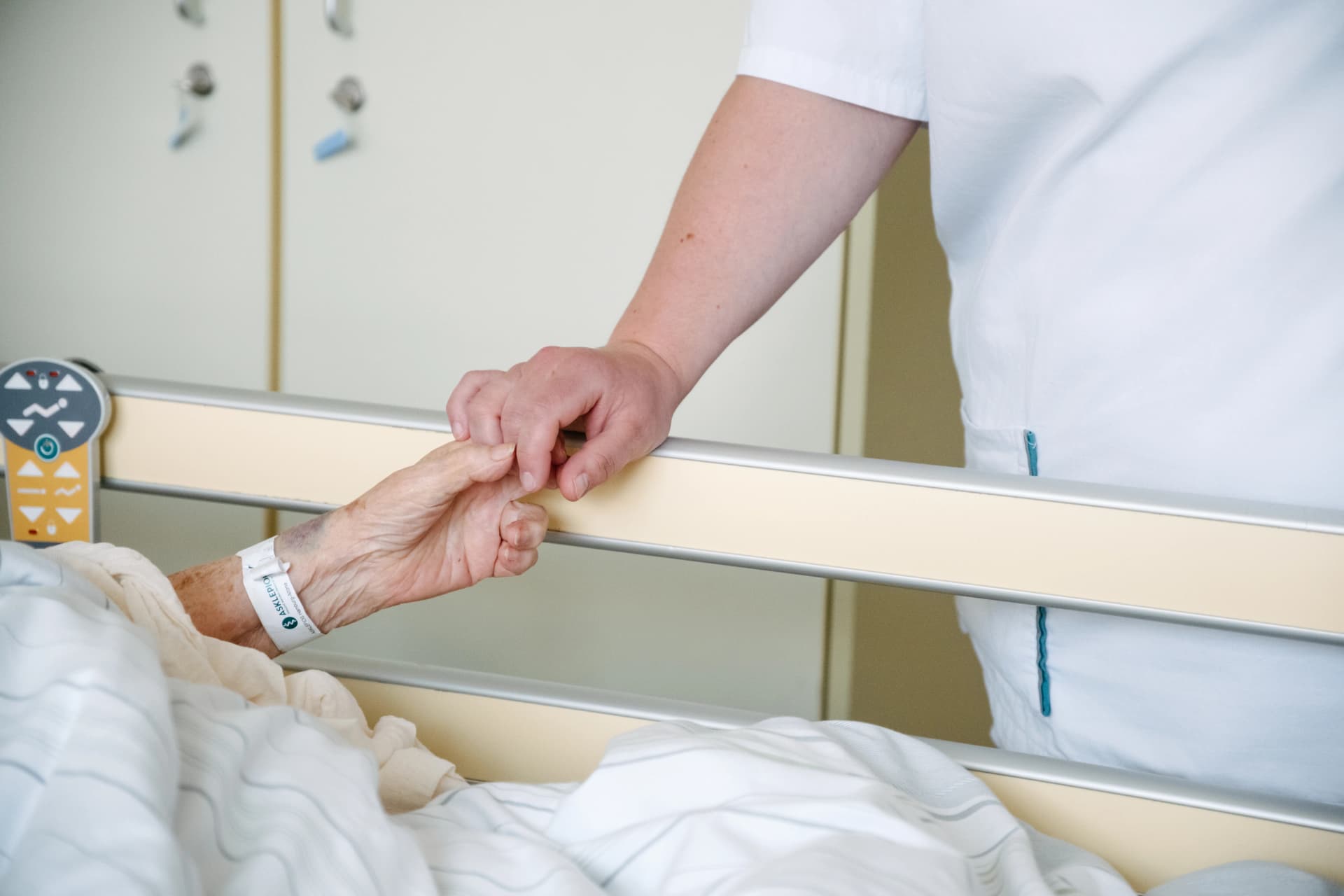 Pflegekraft hält einer Patientin über die Bettkante die Hand