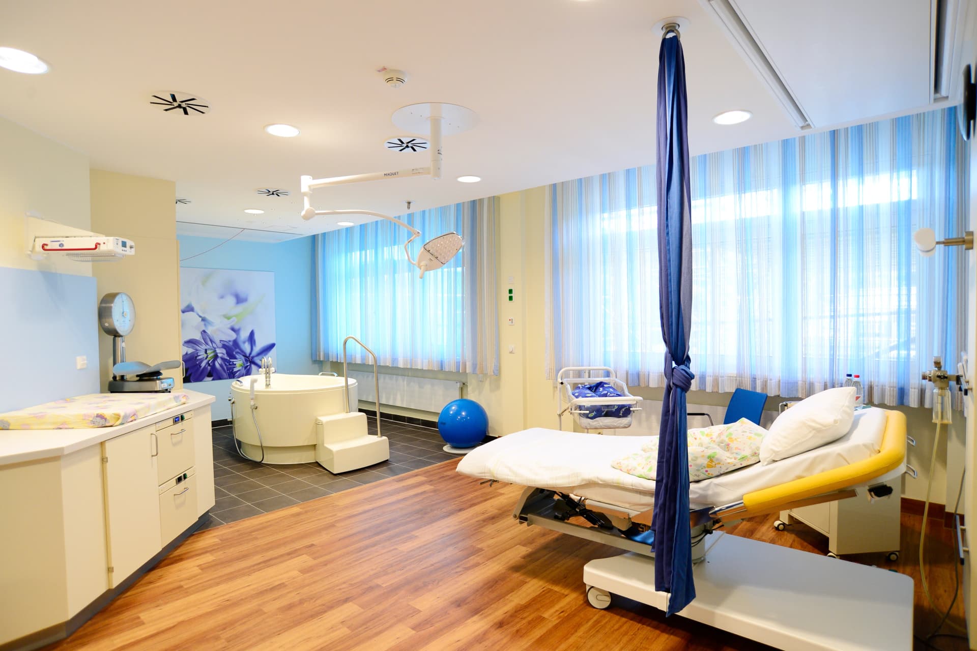 Alt: Unser großer Kreißsaal 3 mit Gebärwanne und einem Bett, zwei Fenstern und blauer Wand