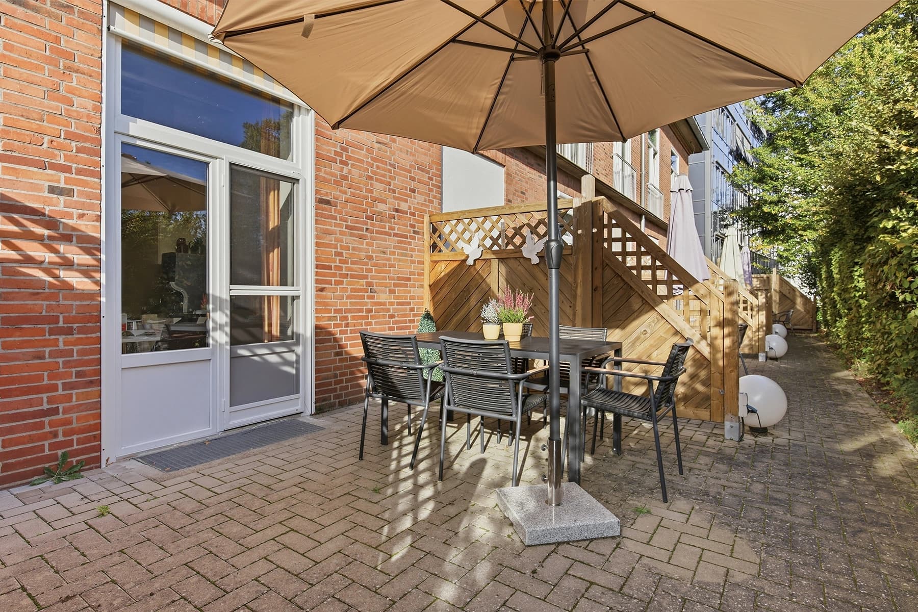 Das Bild zeigt eine Terrasse mit Tisch, Stühlen und Sonnenschirm