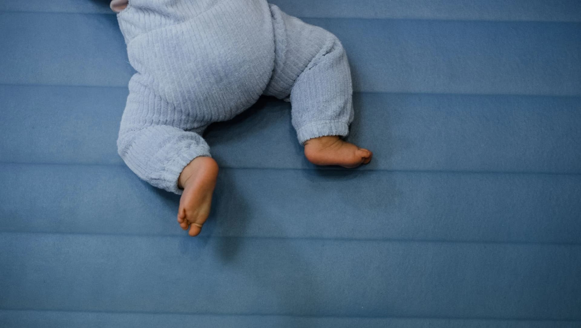 Baby krabbelt auf einer blauen Turnmatte aus dem Bild. Man sieht nur die Füße und den Windelpo.
