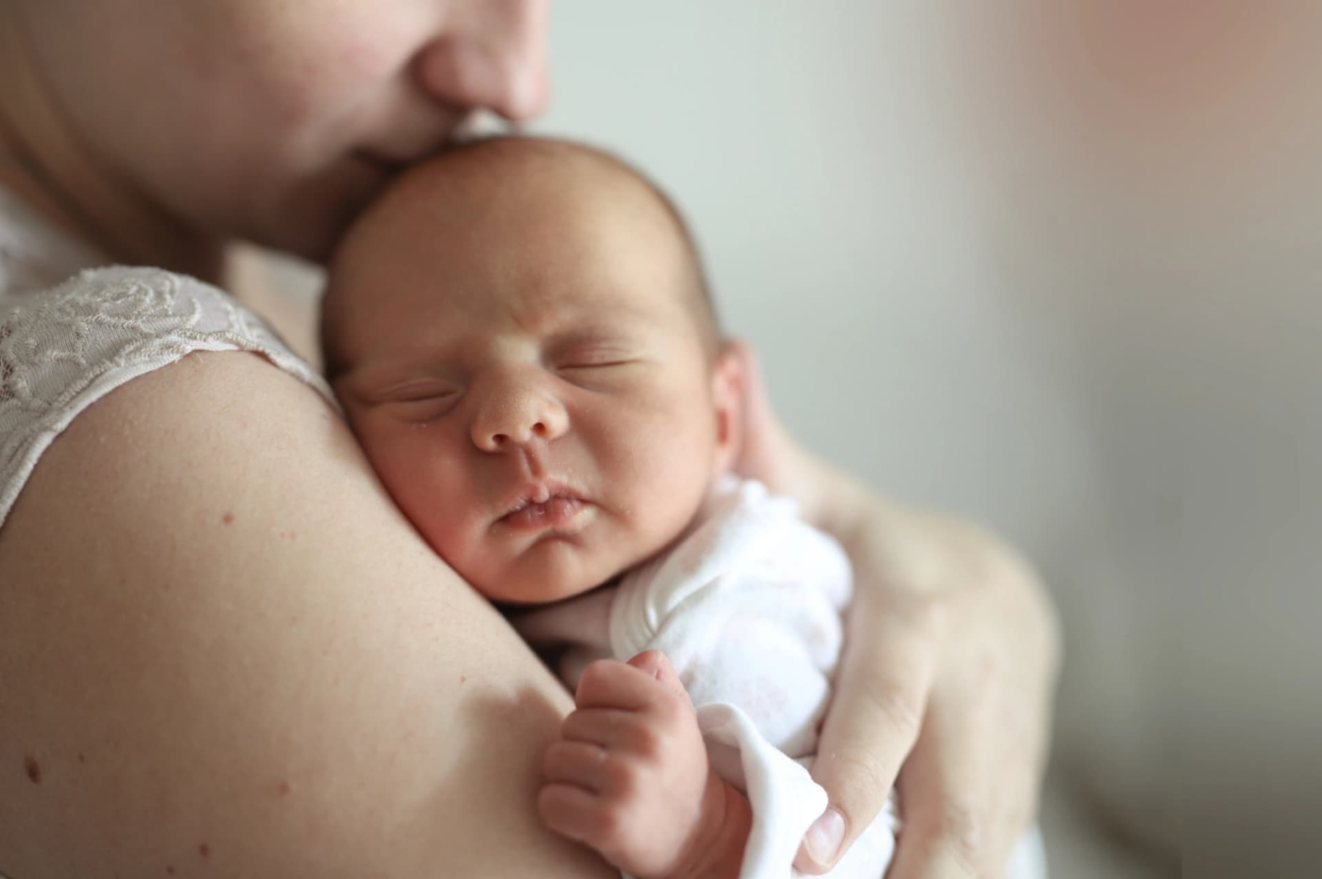 Großaufnahme einer Mutter, die ein schlafendes Baby im Arm hält und es vorsichtig auf den Kopf küsst