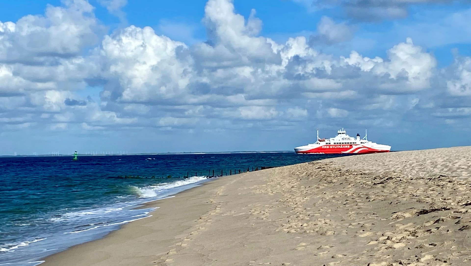 Das Bild zeigt die rot-weiße Syltfähre im Meer vor dem Strand in List.