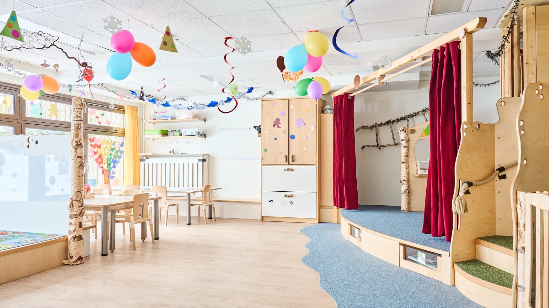 Bild: Gruppenraum mit Treppen, Vorhängen und Nischen, die verschiedene Funktionsecken für freies Spiel schaffen.