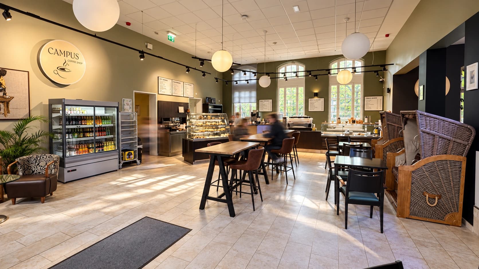 Innenbereich des Campus-Cafés Ochsenzoll mit Kaffeebar, Kuchenvitrine, Sitzgelegenheiten und bewegungsunscharfen Personen.