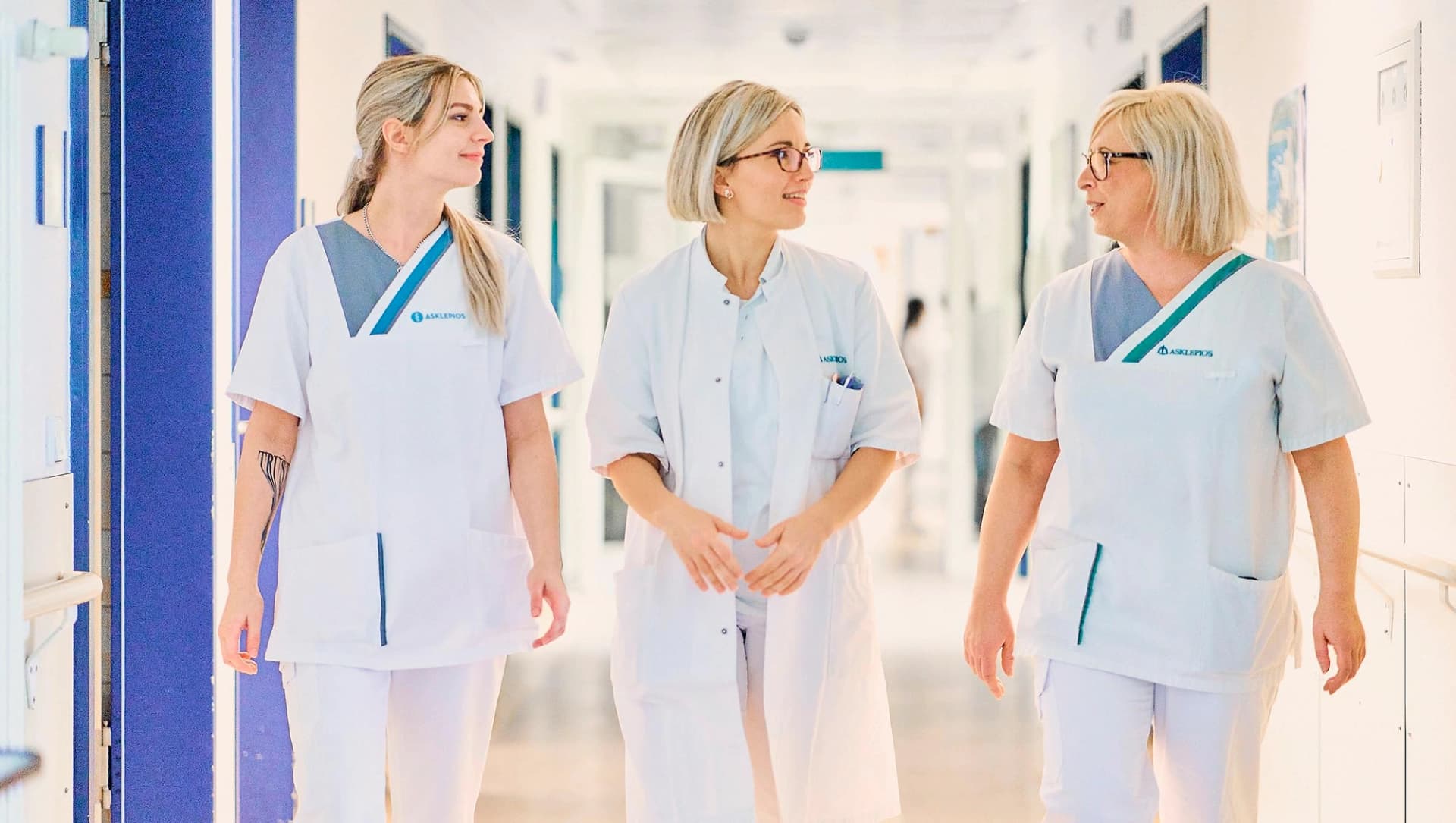 Das Bild zeigt 2 Pflegekräfte und eine Ärztin im Klinikflur