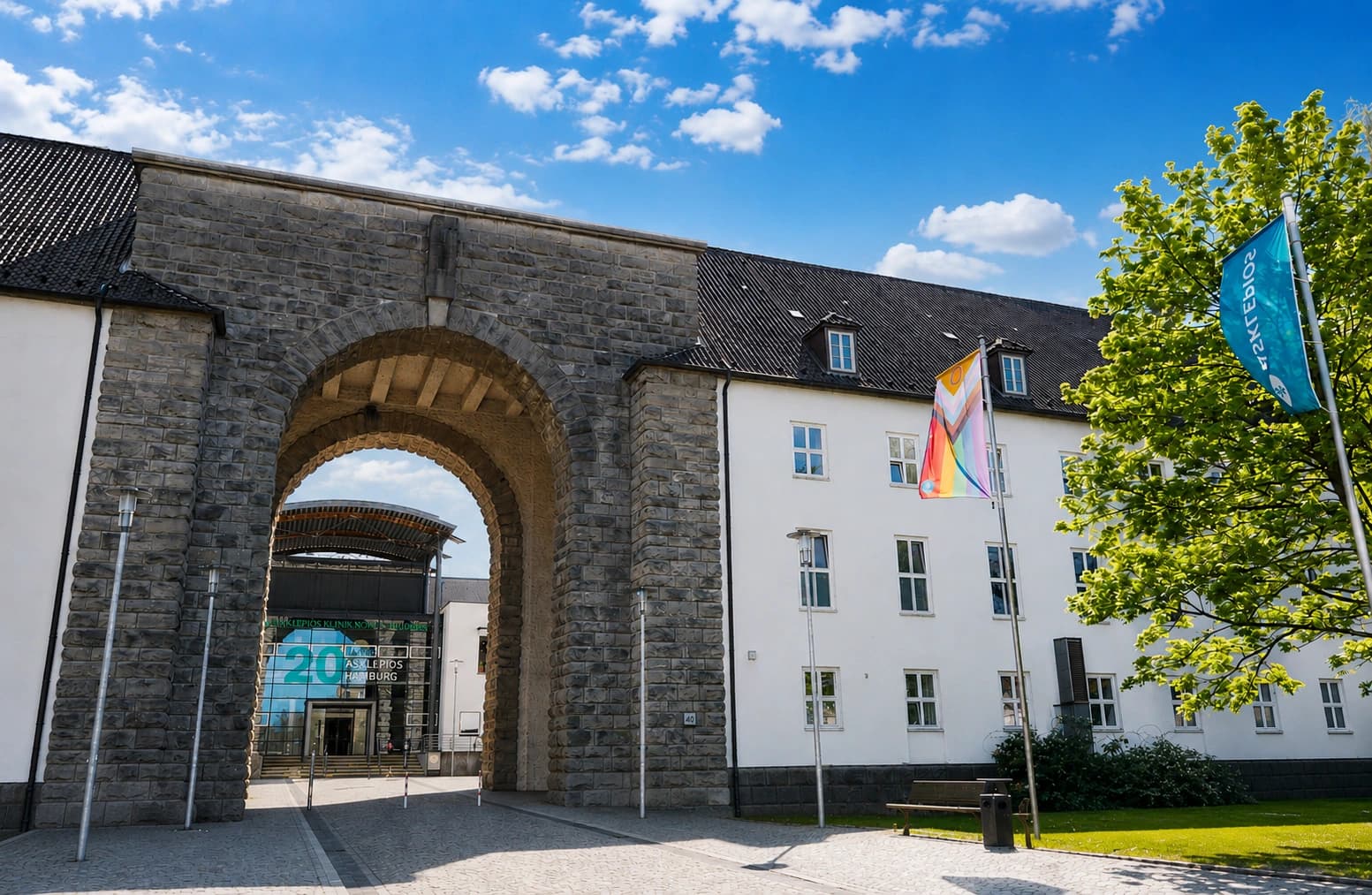 Außenfoto des historischen Eingangsbereichs der Asklepios Klinik Nord – Heidberg in Hamburg mit blauem Himmel und Wolken