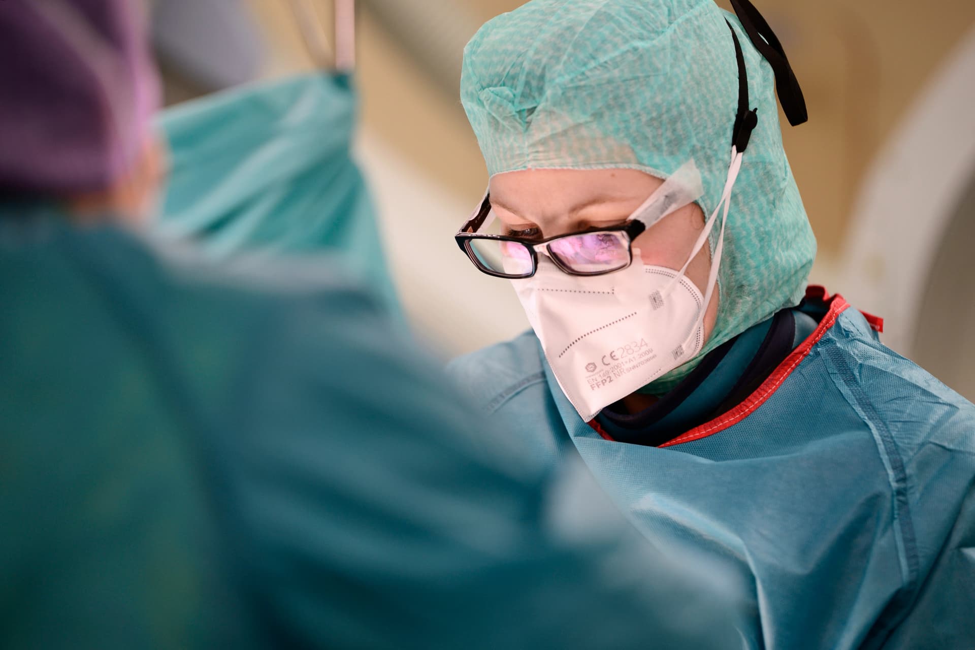 Text: Einblick in Operation mit Nahaufname einer konzentrierten Ärztin in blauer OP-Kleidung und Brille
